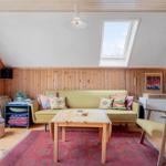 Wohnzimmer mit Sofa, Tisch und Sessel unter Dachschräge mit Fenster.