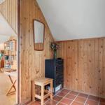 Holzwand, Spiegel, Schrank und Stuhl im Eingangsbereich. Im Hintergrund Wohnzimmer mit Sitzgelegenheit.