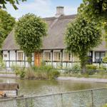 Haus mit Strohdach und Holzrahmen am Wasser mit kleinen Boot.