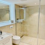 Badezimmer mit Dusche, Waschbecken und Toilette. Beleuchtetes Spiegel und Steinfliesen.