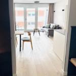 Wohnbereich mit Sofa, Tisch und Stühlen. Balkon mit Sitzgelegenheit. Holzboden und Küchenzeile.
