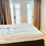 Schlafzimmer mit Bett, TV und Fenster mit Vorhängen.