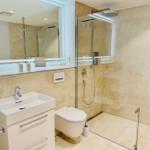 Bad mit Dusche, Waschbecken und Toilette. Fliesenwand und Spiegel.