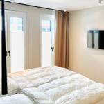 Schlafzimmer mit Bett, TV und Fenstern mit Vorhängen.