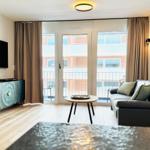Wohnzimmer mit Sofa, Fernseher und Balkonzugang.