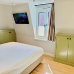 Schlafzimmer mit Bett, TV und Fenster. Grüne Schränke und Holzboden.