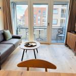 Wohnzimmer mit Sofa, Couchtisch und Balkon. Holzboden und Fernseher sichtbar.