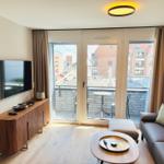 Wohnzimmer mit Sofa, Couchtisch und TV. Balkon mit Tisch und Stühlen. Blick auf Stadt.