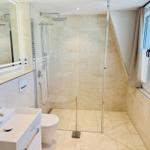 Badezimmer mit Dusche, Waschbecken und Toilette. Fenster mit Vorhängen.