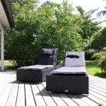 Two black sun loungers on a wooden terrace with green surroundings.