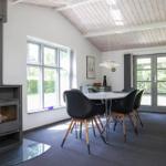 Dining room with wooden ceiling, table, chairs, and wood stove. Windows and glass doors provide ample light.