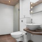 Bad mit Dusche, Toilette und Waschbecken auf Holzunterlage.