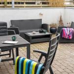 Terrasse mit Gartenmöbeln, Tisch und Stühlen. Beleuchtung an der Wand. Pflanzen und Decken.