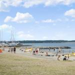 Strand mit Booten, Menschen und Rettungswache unter blauem Himmel.