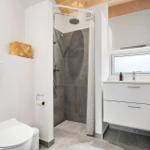 Badezimmer mit Dusche, Waschbecken und Toilette. Holzdecke und weiße Flächen.