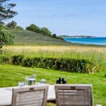 Terrasse mit Tisch und Stühlen, Blick auf Grasland und Meer.