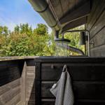 Außendusche mit Dachüberstand und Blick auf grüne Bäume.