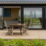 Terrasse mit Holztisch und Stühlen. Blick in Wohnzimmer mit Sofa und Wandbild.