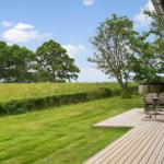 Terrasse mit Sitzgelegenheiten und Blick auf grünes Feld und Bäume.