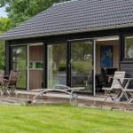 Moderne Holzhütte mit Terrasse, Gartenmöbeln und Blick in den Innenraum.