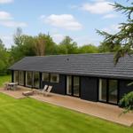 Moderne schwarze Hütte mit Terrasse und Garten. Große Fensterfront mit Sitzgelegenheiten.