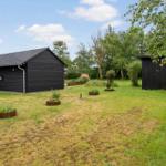 Schwarzes Haus mit Garten und kleinem Nebengebäude unter blauem Himmel.