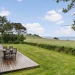 Terrasse mit Tisch und Stühlen, Blick auf Grünland und Meer.