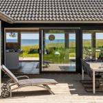 Terrasse mit Liegestuhl und Tisch. Durchgehende Glasfront mit Blick auf Strand und See.