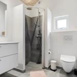 Badezimmer mit Dusche, Waschbecken und Toilette. Holzdecke und Fenster.