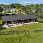 Moderne Villa mit großem Holzterrasse und Garten. Umgeben von Bäumen und Grünflächen.