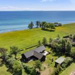 Haus mit Garten und Meerblick. Grünfläche, Bäume und Strand sind sichtbar.