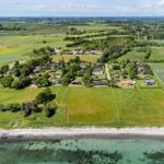 Aerial view of a coastal village with green fields and scattered houses near the sea.