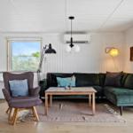 Wohnzimmer mit grünem Sofa, Holztisch und Stühlen. Küche mit Bar und Fenster.