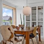Esszimmer mit Holztisch, Stühlen und Glaswand. Fenster mit Blick auf Dach. Deckenleuchte und Wandbild.