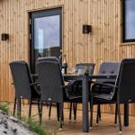 Terrasse mit Tisch und Stühlen vor Holzhäusern mit Fenstern.