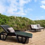 Terrasse mit Liege und Sofa vor grüner Dünenlandschaft.