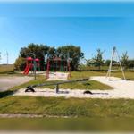 Kinderfreier Spielplatz mit Rutsche, Schaukel und Klettergerüst auf Sandfläche.