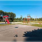 Kinderspielplatz mit Rutsche, Schaukel und Klettergerüst. Hintergrund mit Windrädern und Bäumen.