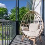 Terrasse mit Rattan-Sessel und Blick auf grüne Bäume.