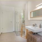 Badezimmer mit Dusche, Waschbecken und Spiegel.