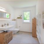 Badezimmer mit Waschbecken, Toilette und Fenster. Holzregale und Wandbilder.