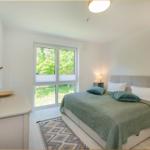 Schlafzimmer mit Bett, Fenster und Schrank. Grün-weiße Bettwäsche und Teppich.