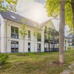 Modernes Mehrfamilienhaus mit Balkonen und begrüntem Außenbereich.