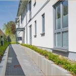 Gehweg neben modernem Haus mit Fenstern und Grünflächen.