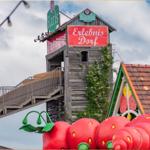 Erlebnis Dorf mit großen Erdbeeren und Holzgebäude unter bewölktem Himmel.