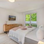 Schlafzimmer mit Bett, Schrank und TV. Fenster mit Blick auf Grün.