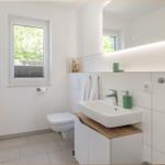 Badezimmer mit Waschbecken, Toilette und Fenster. Spiegelschrank mit beleuchteter Oberseite.