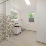 Badezimmer mit Dusche, Waschbecken und Toilette. Fenster mit Blick auf Grün.