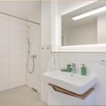 Bad mit Dusche, Waschbecken und beleuchtetem Spiegel