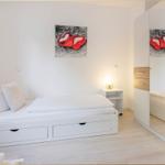 Schlafzimmer mit weißem Bett, Spiegelschrank und Wandbild mit roten Herzen.